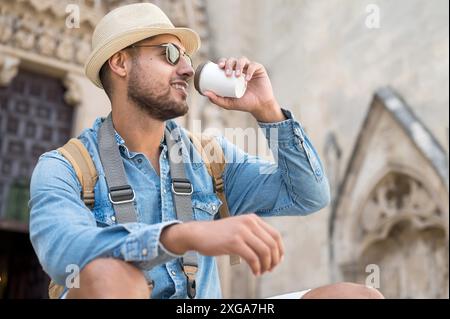 Un jeune touriste heureux avec un café à emporter et un sac à dos reposant dans la rue. Photo de haute qualité Banque D'Images