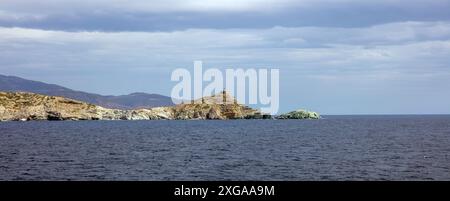 Île d'Andros, Cyclades Grèce. Phare sur un énorme rocher au-dessus de l'eau de mer égéenne ondulée. Balise sur la falaise pour la navigation, ciel nuageux. Bannière Banque D'Images