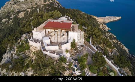 Drone shot, Un bâtiment avec un toit rouge entouré d'arbres sur une colline près de la mer, église Panagia Kyra, au-dessus de la plage de Tsambika, point de vue, Tsambika Banque D'Images