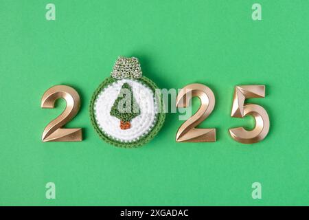 Jouet tricoté pour arbre de Noël et numéros d'or. Le symbole de l'année 2025 sur fond gris. Banque D'Images