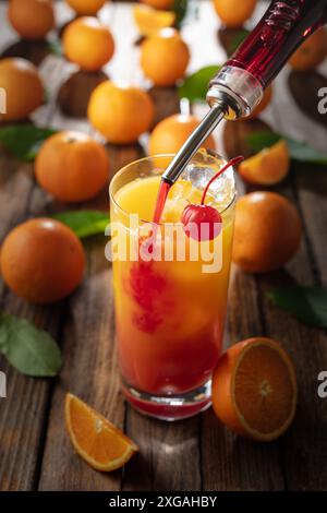 Cocktail classique de tequila au lever du soleil, superposé de tequila aux teintes vibrantes de jus d'orange et de grenadine, garni d'une brochette de cerises maraschino. La grenadine est po Banque D'Images