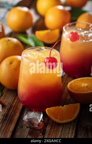 Cocktail classique de tequila au lever du soleil, superposé de tequila aux teintes vibrantes de jus d'orange et de grenadine, garni d'une brochette de cerises maraschino. Banque D'Images