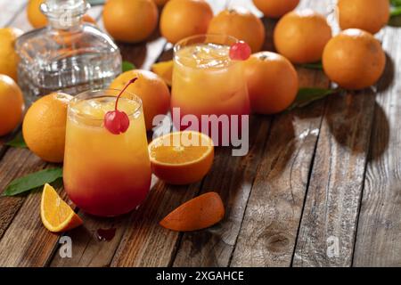 Cocktail classique de tequila au lever du soleil, superposé de tequila aux teintes vibrantes de jus d'orange et de grenadine, garni d'une brochette de cerises maraschino. Banque D'Images