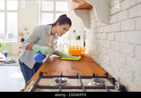 Jeune femme au foyer portant des gants de protection en caoutchouc dans la table de travail de nettoyage de cuisine moderne, en utilisant un chiffon Banque D'Images