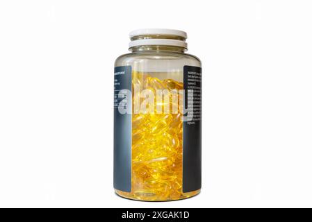 Un flacon en verre avec un bouchon blanc est rempli de gélules jaunes. La bouteille a une étiquette noire avec un lettrage blanc. Banque D'Images