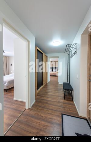 Hall d'entrée de la maison. Intérieur. Porte blanche en bois, plancher brun et armoire blanche. Minimalisme. Voyant LED. Banc noir. Miroir Banque D'Images