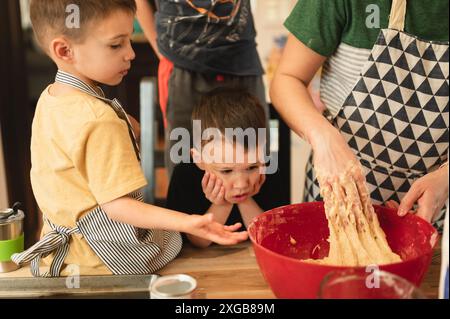 Les jeunes garçons attendent impatiemment que maman finisse de mélanger la pâte à biscuits Banque D'Images