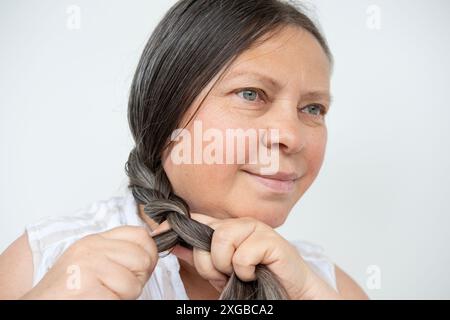 heureuse femme mature sourit, étant tressé de longs cheveux bruns, appréciant moment de soins personnels, l'acceptation de soi et le vieillissement de voyage avec grâce et dignité Banque D'Images
