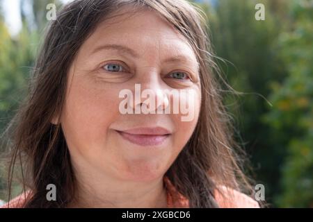 une femme de 55 ans sourit, ses yeux aimables regardent heureux, le visage en gros plan, la bonne humeur, les changements liés à l'âge, le concept de santé mentale humaine, l'optimisme chez l'adulte Banque D'Images