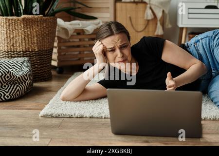 Une femme en introspection, allongée sur le sol fixée sur son écran d'ordinateur portable. Banque D'Images