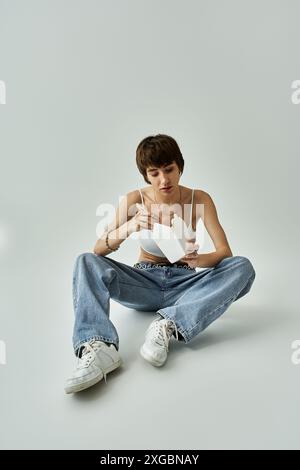 Jeune femme dans une tenue élégante mangeant paisiblement des nouilles tout en étant assise sur le sol. Banque D'Images