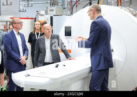 Erlangen, Allemagne. 08 juillet 2024. Le chancelier allemand Olaf Scholz (au centre, SPD) se tient devant un scanner IRM en cours de test final avec Andreas Schneck (à gauche), responsable IRM, et Bernd Montag (à droite), PDG de Siemens Healthineers AG, lors d'une visite sur le site de production d'imagerie par résonance magnétique (IRM) de Siemens Healthineers AG. Crédit : Daniel Karmann/dpa/Alamy Live News Banque D'Images