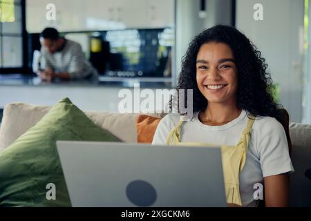 Une femme sourit en utilisant un ordinateur portable sur le canapé dans la chambre Banque D'Images