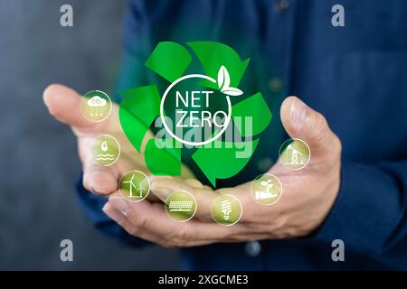 Un homme dans une chemise bleue tient un symbole de recyclage vert avec les mots net zero. Le symbole de recyclage a une plante dessus, suggérant que le recyclage aide Banque D'Images