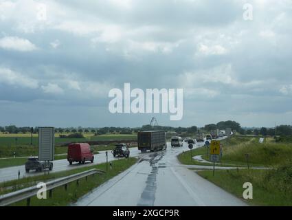 PRODUCTION - 03 juillet 2024, Schleswig-Holstein, Burg Auf Fehmarn : voitures et camions roulent vers le sud sur la route fédérale B 207 sur l'île de Fehmarn. La construction de la liaison Fehmarn Sound et Fehmarn Belt progresse. Le tunnel de 55,1 milliards de couronnes (environ 7,4 milliards d'euros) reliera l'île danoise de Lolland à l'île allemande de Fehmarn et sera composé de 89 éléments en béton, qui seront construits dans une usine spéciale à Rödbyhavn sur Lolland. Avec 18 kilomètres, le tunnel immergé le plus long du monde selon la société Sund & Baelt se compose d’une route à quatre voies et d’un chemin de fer Banque D'Images