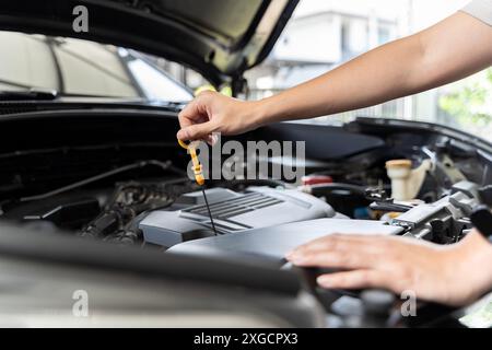 Photo en gros plan de la main de la femme vérifier l'huile moteur Une femme sort la jauge pour vérifier le niveau d'huile de sa voiture. Femme réparant la voiture dans le garage ou le wor Banque D'Images