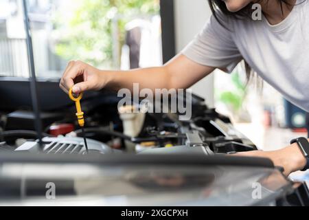 Photo en gros plan de la main de la femme vérifier l'huile moteur Une femme sort la jauge pour vérifier le niveau d'huile de sa voiture. Jeune femme occasionnelle travaillant avec la voiture Banque D'Images