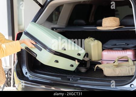 Femme chargeant la valise dans le coffre de voiture, préparation pour le voyage. Coffre de voiture ouvert emballé pour des vacances en famille. Jeune belle femme concept de voyage féminin ta Banque D'Images