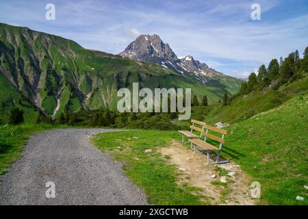 Panorama avec un banc de parc sur un sentier de randonnée avec vue sur les montagnes environnantes dans la région d'Arlberg, sommets nuageux enneigés Banque D'Images