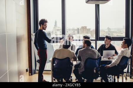 Groupe d'arhitecture mâle multiethnique des concepteurs en vêtements de loisirs autour de la table dans un bureau moderne, le jeune homme de race blanche le président representi Banque D'Images