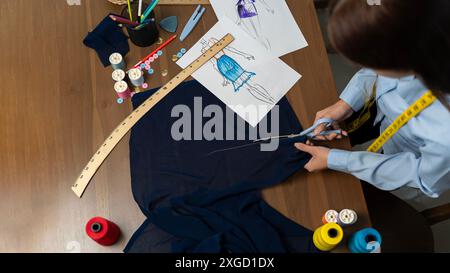 Un tailleur coupe une robe sur une ligne de croquis avec une machine à coudre, un créateur de mode fait une robe ou des égouts dans un studio, un atelier conçoit des vêtements, un nouveau Banque D'Images