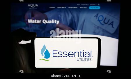 Personne tenant le téléphone portable avec le logo de la société US de services publics de l'eau Essential Utilities Inc en face de la page Web de l'entreprise. Concentrez-vous sur l'affichage du téléphone. Banque D'Images
