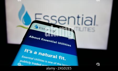 Téléphone portable avec page Web de la société américaine de services publics de l'eau Essential Utilities Inc devant le logo de l'entreprise. Concentrez-vous sur le coin supérieur gauche de l'écran du téléphone. Banque D'Images