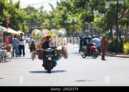 Hoi an, Vietnam 7 juillet 2024 : le colporteur vend ses chapeaux coniques vietness sur la moto. La vieille ville est un port commercial d'Asie du Sud-est datant du 15t Banque D'Images