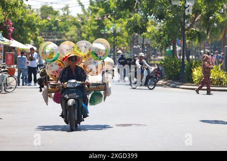 Hoi an, Vietnam 7 juillet 2024 : le colporteur vend ses chapeaux coniques vietness sur la moto. La vieille ville est un port commercial d'Asie du Sud-est datant du 15t Banque D'Images