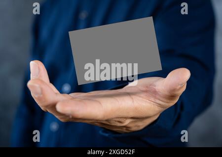 Homme tenant une carte de visite gris foncé contre un mur de béton main masculine mature tenant une carte de visite vierge devant la caméra. Backgroun flou Banque D'Images