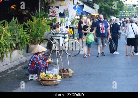 Hoi an, Vietnam 7 juillet 2024 : hawker vend les fruits dans la rue. La vieille ville de Hoi an est un port de commerce d'Asie du Sud-est datant du 15ème au 19ème siècle Banque D'Images