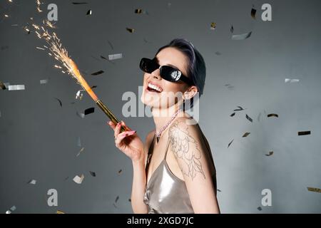 Femme élégante avec les cheveux bleus courts portant des lunettes de soleil, tenant Sparkler. Banque D'Images