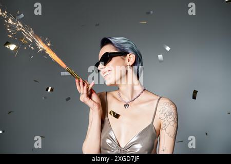 Jeune femme aux cheveux courts bleus tient élégamment un étincelant, habillé dans une tenue argentée glamour dans un cadre de studio. Banque D'Images