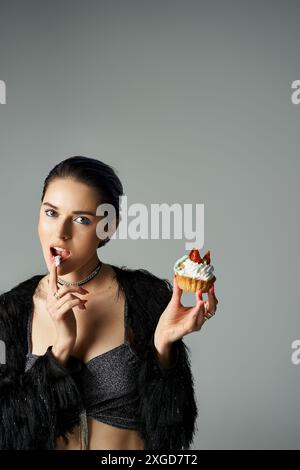 Une jeune femme élégante aux cheveux teints pose avec un cupcake, en prenant une bouchée. Banque D'Images