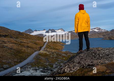 Homme en manteau de pluie jaune regardant le col de montagne, les montagnes glaciaires et les lacs d'eau de fonte, parc national de Jotunheimen, Norvège, Scandinavie, Europe Banque D'Images