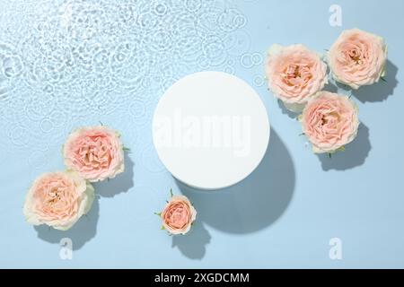 Belles fleurs de rose et podium de forme ronde dans l'eau sur fond bleu clair, pose plate Banque D'Images