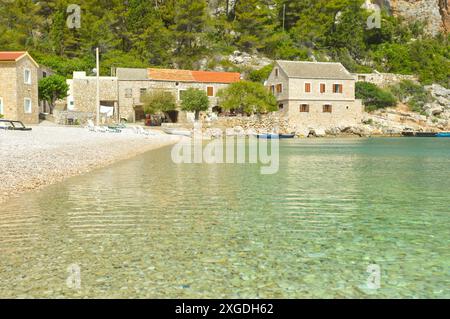 Belle plage de galets Veliki Pokrivenik à l'île de Hvar avec des maisons en pierre sur le rivage Banque D'Images