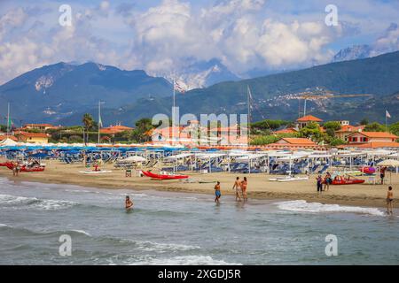 Belle plage avec nageurs et bains de soleil à forte Dei Marmi, Italie. Alpes Apuanes en arrière-plan. Parasols et chaises longues bordant la plage. Banque D'Images