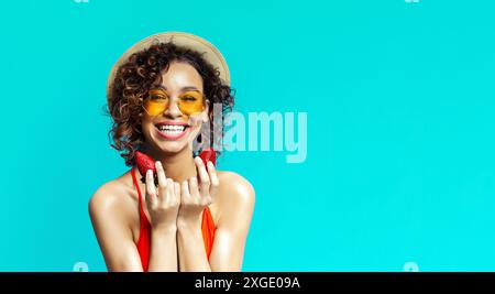 Femme souriante en bikini rouge tient des fraises sur fond bleu Banque D'Images