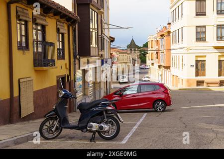 Astorga, Espagne - 3 juin 2023 : une voiture rouge est garée dans une rue étroite d'Astorga, Espagne. Un scooter noir est garé à proximité. Bâtiments jaune vif l Banque D'Images