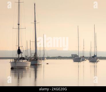 Groupe de voiliers amarrés dans le plan d'eau. North Solent Stuary, Hampshire, Royaume-Uni. La scène est calme et paisible, avec les bateaux reflétés sur l'eau Banque D'Images