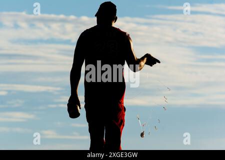 Salvador, Bahia, Brésil - 17 mai 2019 : un pêcheur non identifié, en silhouette, est vu jetant une ligne de nylon avec un appât dans l'eau de Rio Vermelho Banque D'Images