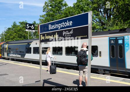 Les gens attendent sur un quai à la gare de Basingstoke pour un chemin de fer du Sud-Ouest, avec un panneau annonçant la maison du Festival place. Angleterre Banque D'Images