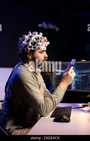 Ingénieur avec casque EEG insérant la cartouche dans le PC pour utiliser un logiciel de haute technologie permettant le transfert du cerveau dans le monde virtuel. Homme mettant le disque dans l'ordinateur pour commencer le téléchargement de conscience Banque D'Images