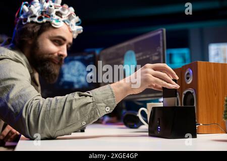 Ingénieur avec casque EEG insérant la cartouche dans le PC pour utiliser un logiciel de haute technologie permettant le transfert du cerveau dans le monde virtuel. Homme mettant le disque dans l'ordinateur pour commencer le téléchargement de conscience Banque D'Images