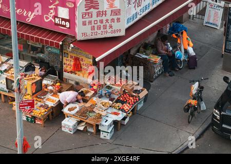 Un épicier expose ses fruits et légumes dans la rue de Chinatown, New York, tandis qu'un livreur attend à proximité avec son vélo et son hi-vis Banque D'Images