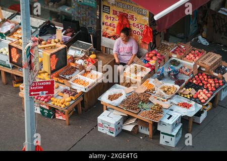 Le propriétaire d'une épicerie chinoise expose des fruits et légumes dans la rue de Chinatown, New York, tandis qu'un livreur attend à proximité Banque D'Images