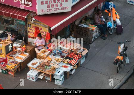 Un épicier expose ses fruits et légumes dans la rue de Chinatown, à New York, tandis qu'un livreur attend à proximité avec son vélo Banque D'Images