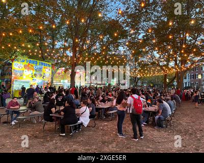 Les gens aiment manger leur dîner de food truck la nuit sous une chaîne de lumières dans un parc public lors d'un festival à Salem, Massachusetts Banque D'Images