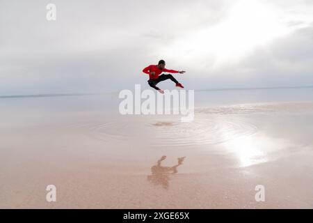 Un homme en chemise rouge saute en l'air au-dessus d'un plan d'eau. L'image a un sentiment de liberté et d'excitation, car l'homme exécute un ju audacieux Banque D'Images